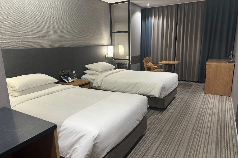 Chambre de motel moderne avec deux lits doubles aux draps blancs immaculés, décoration sobre en gris et bois, idéale pour choisir un motel confortable.