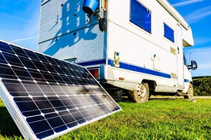 Panneau solaire portable posé sur l'herbe à côté d'un camping-car blanc garé dans la nature pour un week-end en camping-car en Alsace.